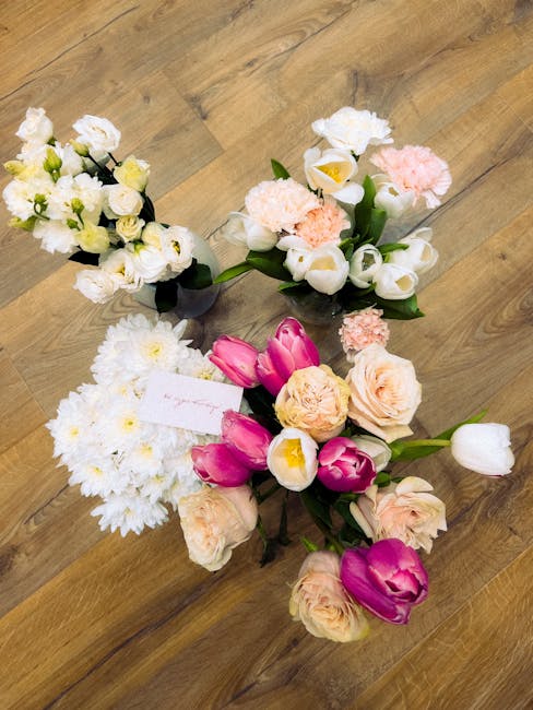 A collection of four hand-arranged floral bouquets placed on a wooden floor, featuring a variety of fresh flowers with vibrant colors. The arrangement includes white roses and small white blossoms in 